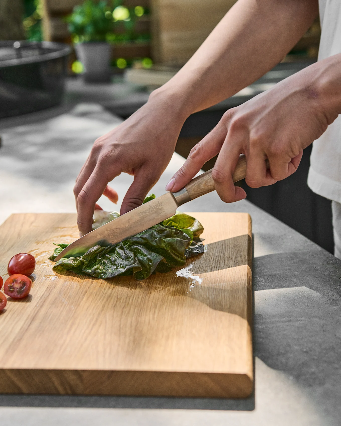 Mains coupant de la laitue verte sur une planche à découper en bois à côté de tomates cerises.