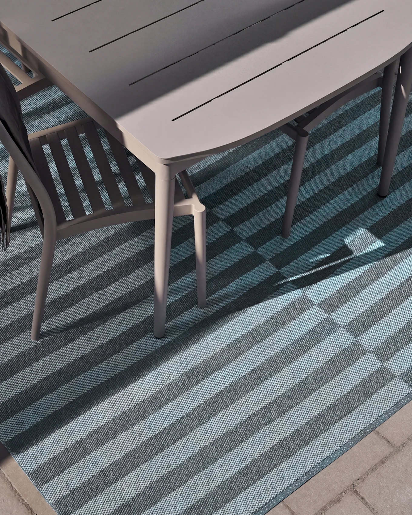 Vue aérienne d'une table et chaise de salle à manger extérieure sur un tapis rayé avec des rayures bleues claires et foncées, partiellement éclairées par le soleil.