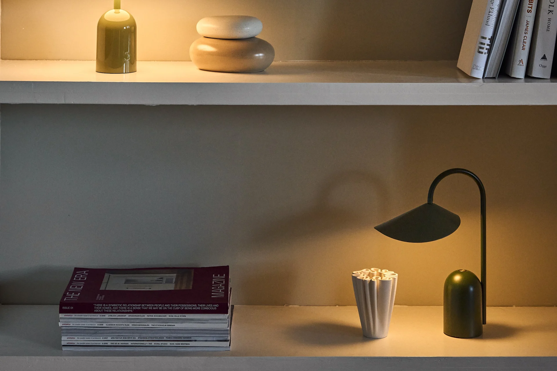 Trois étagères présentent diverses lampes de bureau vertes et violettes, ainsi que des livres, magazines et objets décoratifs.