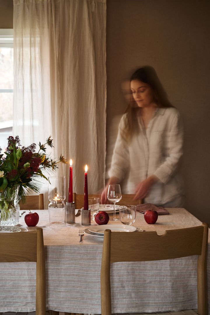 Une femme dresse une table de Noël simple avec des bougies rouges, de la porcelaine de Noël à motifs et une simple nappe rayée. 