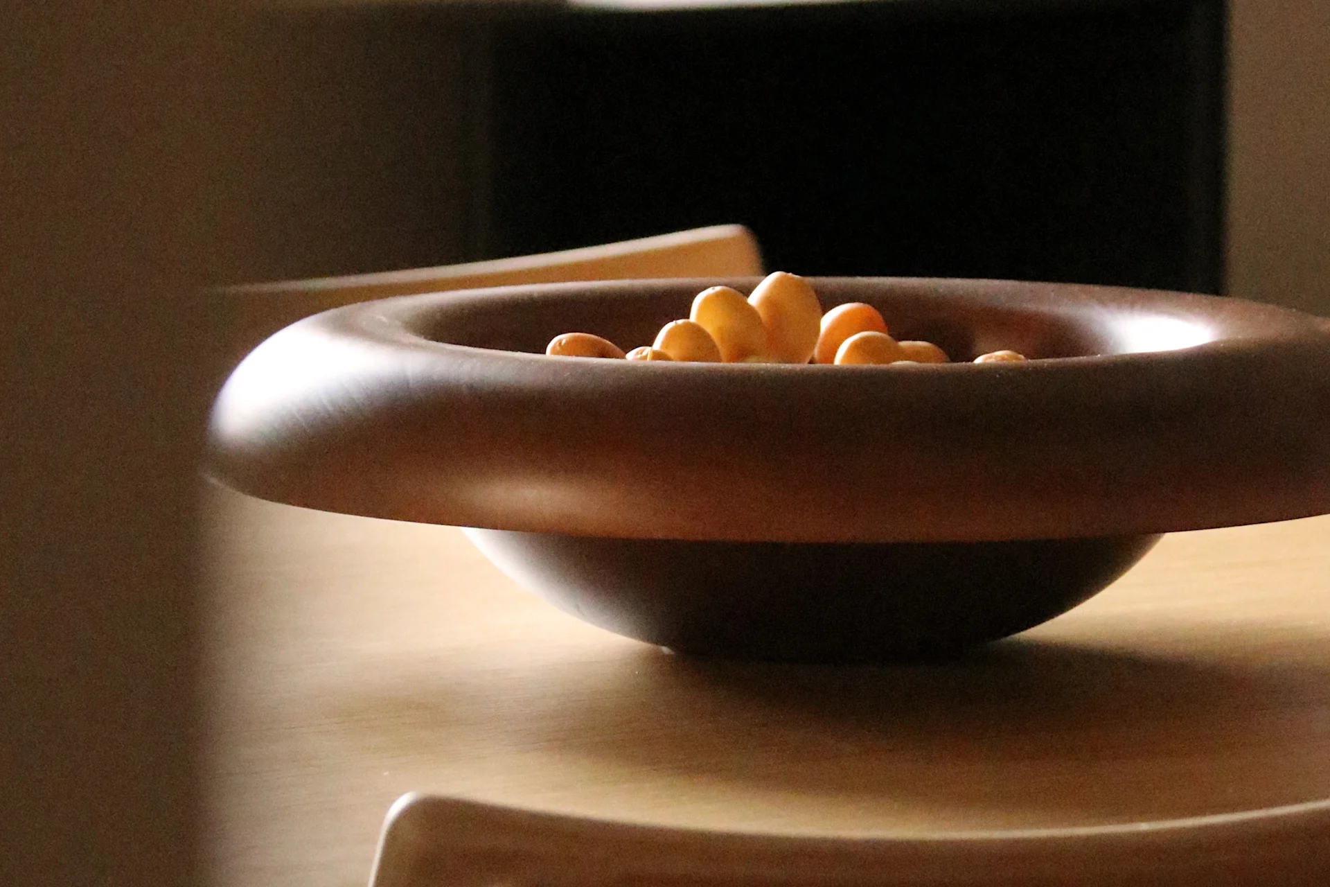 Bol en bois marron foncé à large bord rempli de snacks clairs sur une table en bois clair.