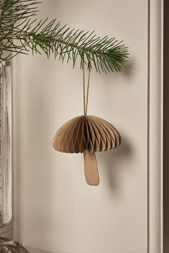 Des idées de décoration de sapin de Noël inspirées de la nature, comme la décoration de champignon Fungi de Broste Copenhagen, que l'on voit ici suspendue à une branche. 