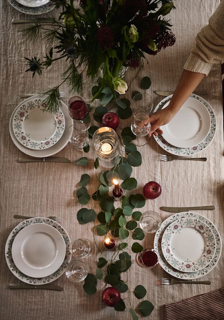 Une idée de table de Noël simple et élégante photographiée du dessus avec des feuilles vertes et des pommes rouges en guise de décoration. 