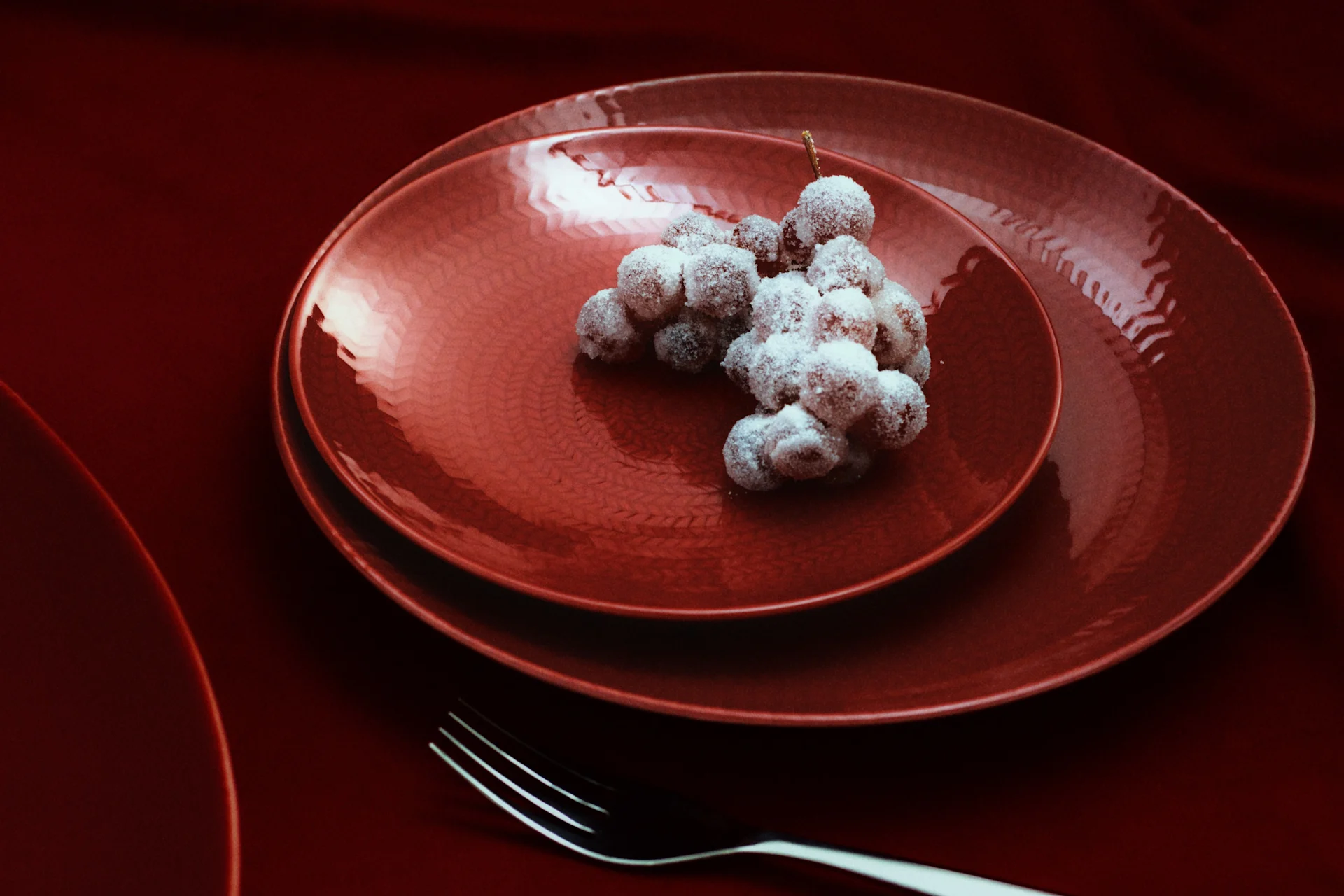 Raisins givrés sur des assiettes rouges texturées avec des fourchettes sur une table rouge foncé.