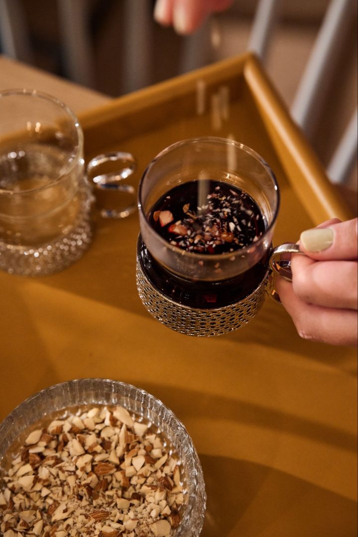 Une main saupoudre des amandes dans un verre de glögg traditionnel sur une table de Noël nordique. 