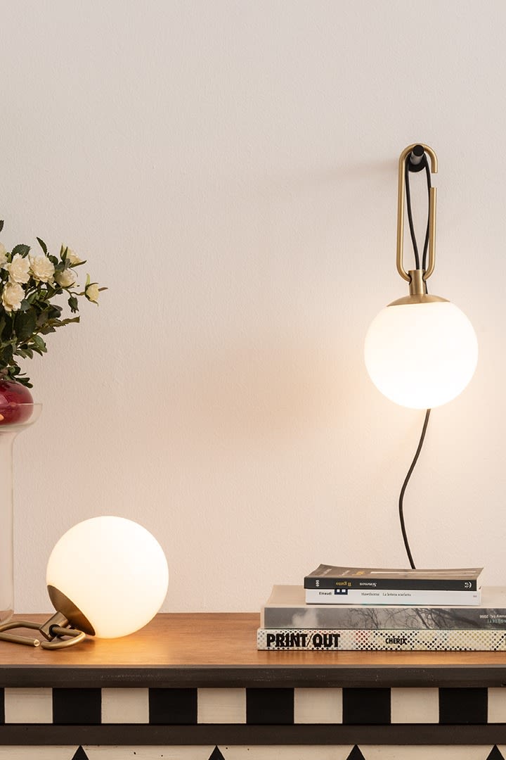 Les lampes murales et de table NH d'Artemide sont suspendues et posées sur un bureau avec une pile de livres.