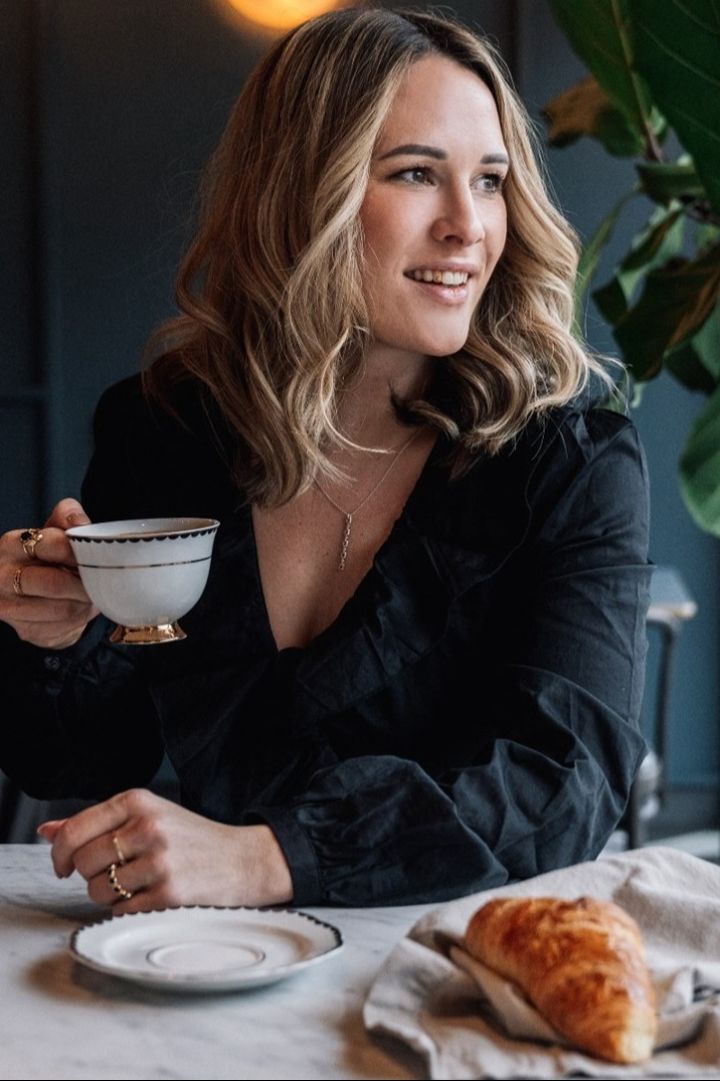 La fondatrice Giovanna Hilke est assise à une table et regarde sur le côté. Elle tient à la main la tasse Lignano Sabbiadoro de Hilke Collection.