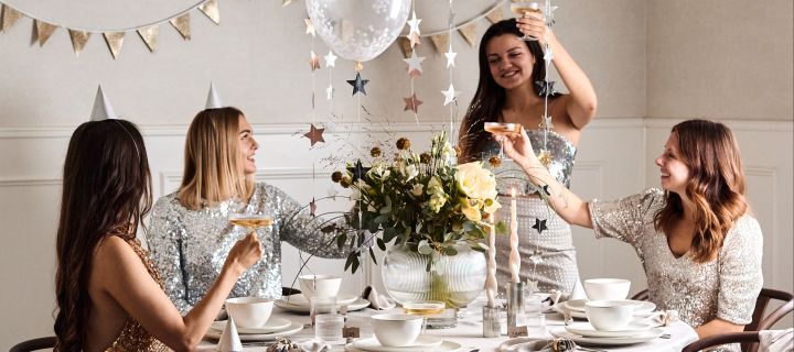 Des idées pour votre fête de la Saint-Sylvestre : vous voyez ici une bouteille décorée d'une écriture scintillante posée sur une table élégamment dressée.