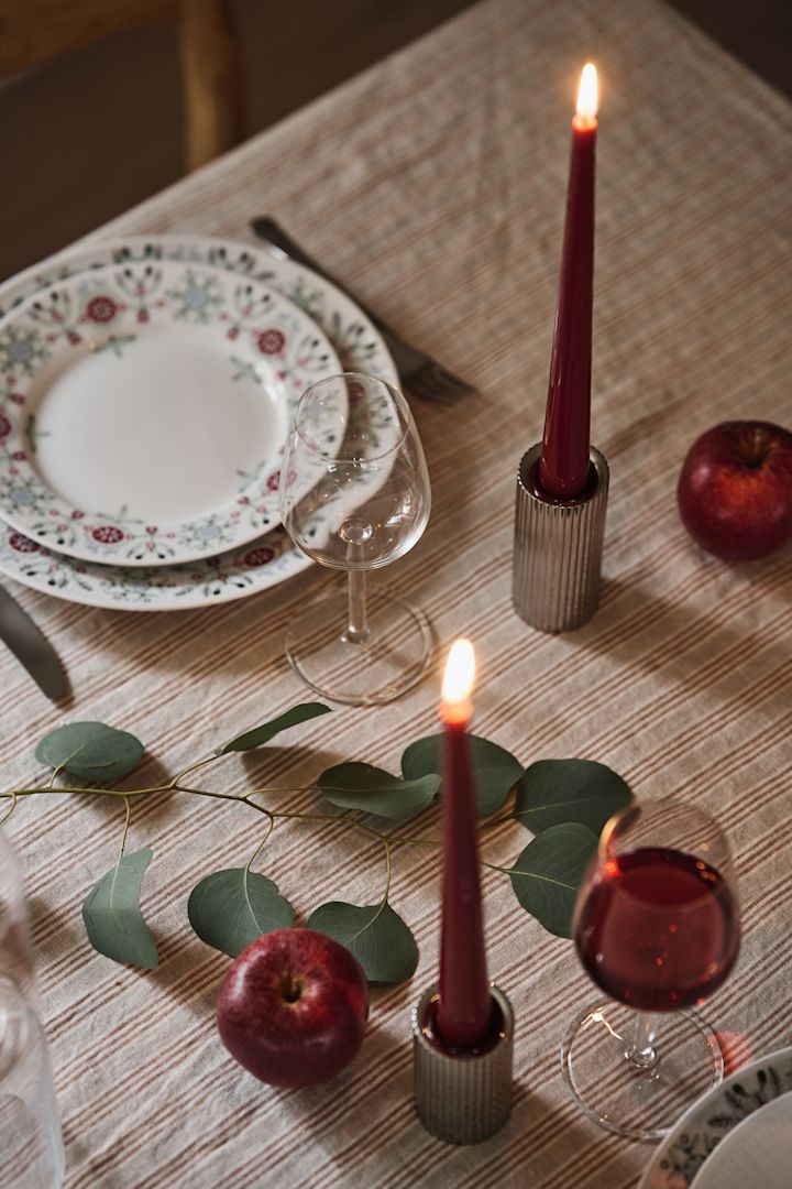 Gros plan sur des bougies rouge foncé dans des bougeoirs chromés, dans le cadre d'une table de Noël simple. 