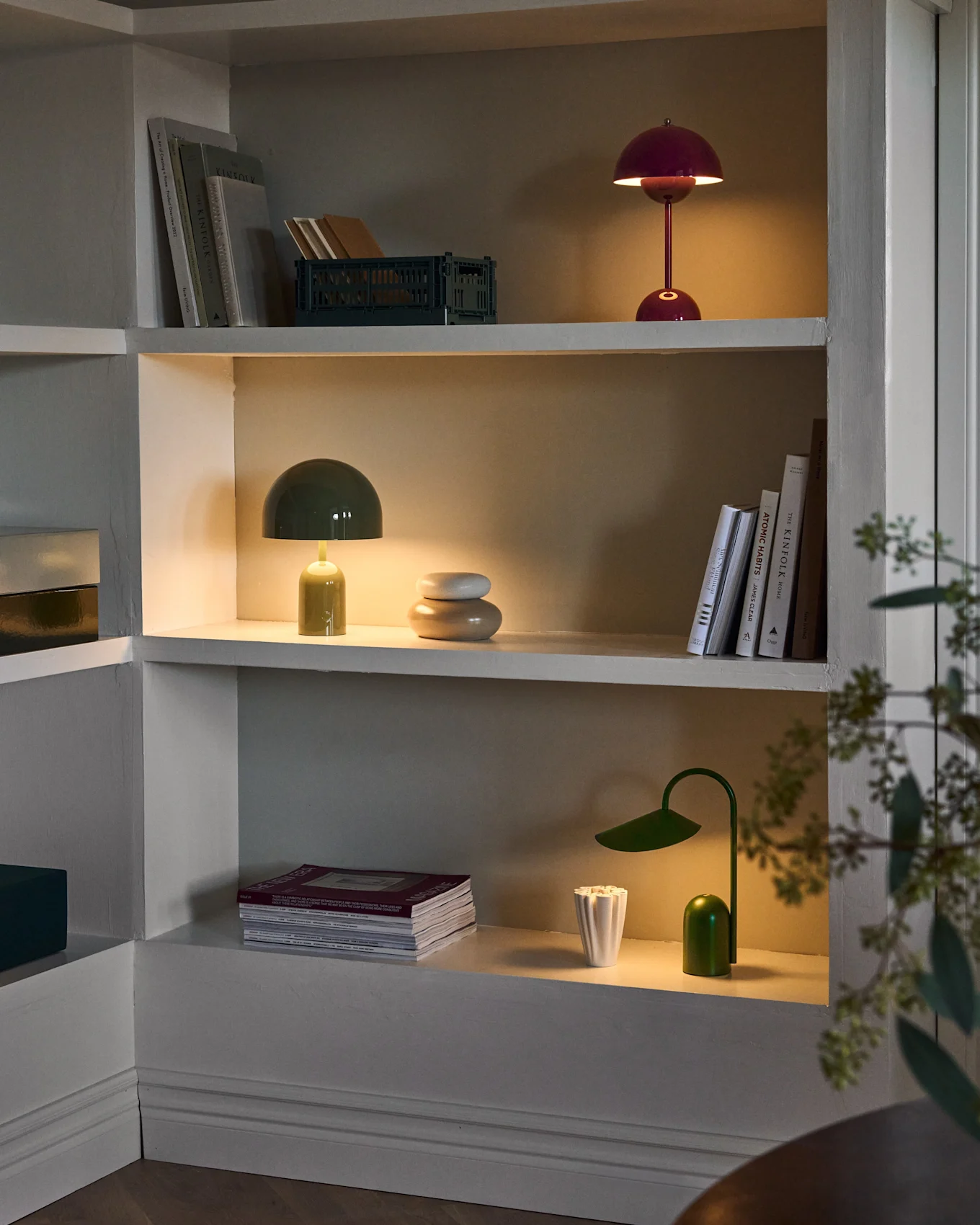 Étagères éclairées dans meuble encastré, avec lampes champignons rouges et vertes, lampe de bureau verte, livres et déco.
