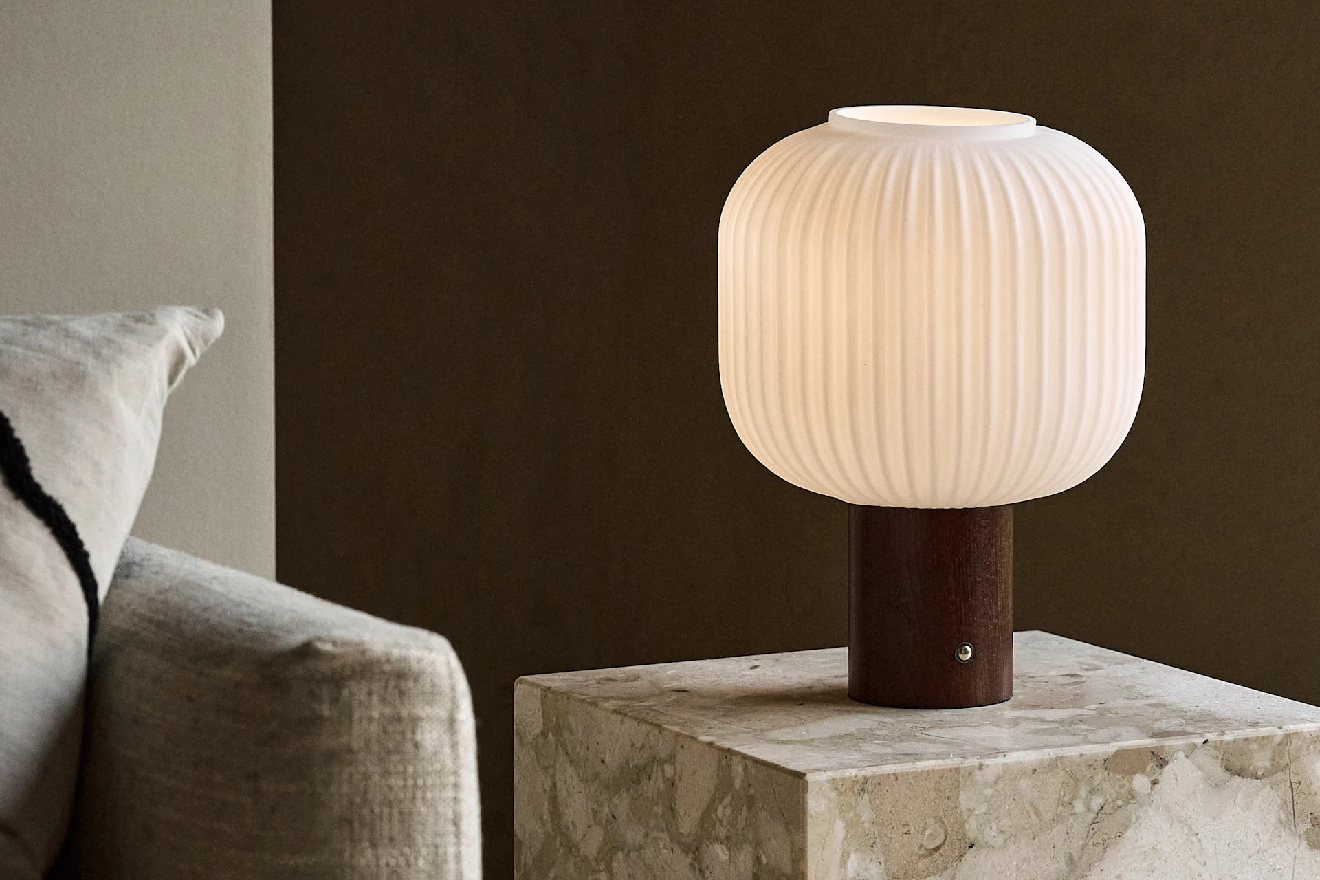 Lampe de table blanche côtelée avec une base en bois sur une table d'appoint en marbre à côté d'un canapé.
