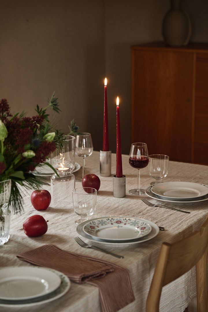 Des bougies de Noël rouges sont disposées sur une table de Noël simple avec des assiettes à motifs et des accents rouges. 