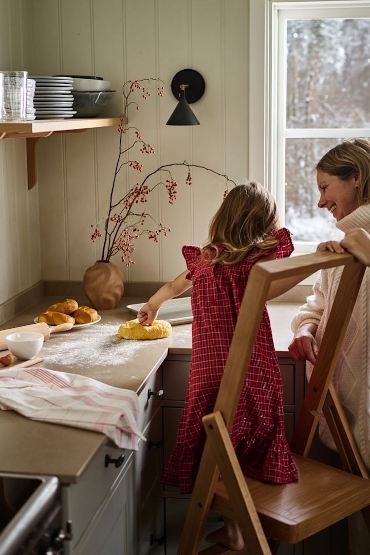 Le Noël su�édois se caractérise aussi par la pâtisserie. Ici, vous voyez une jeune fille en robe rouge, debout sur l'échelle Step de Design House Stockholm dans la cuisine, en train de pétrir la pâte des Lussekatter.