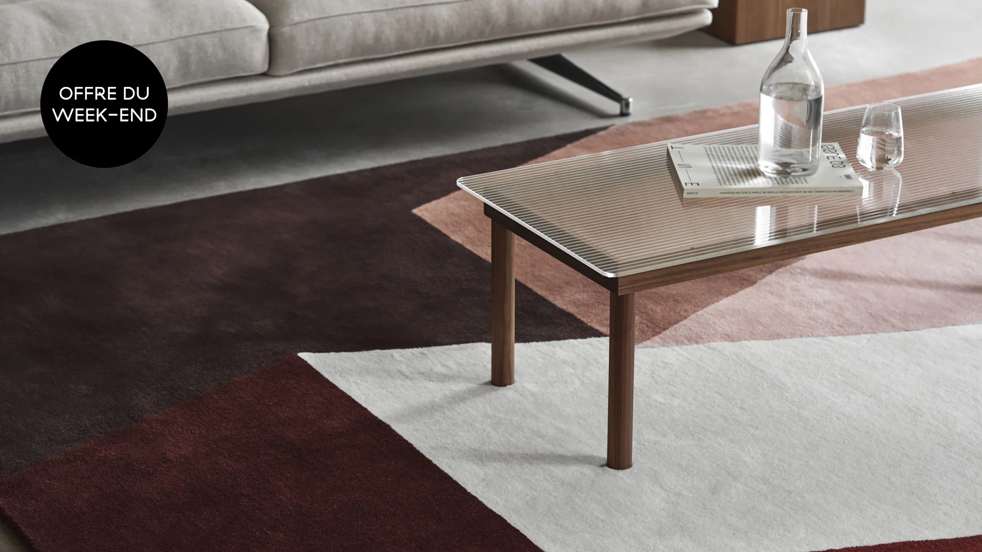 Salon moderne avec un tapis à motifs géométriques, une table basse en verre et une superposition 'WEEKEND DEAL'.