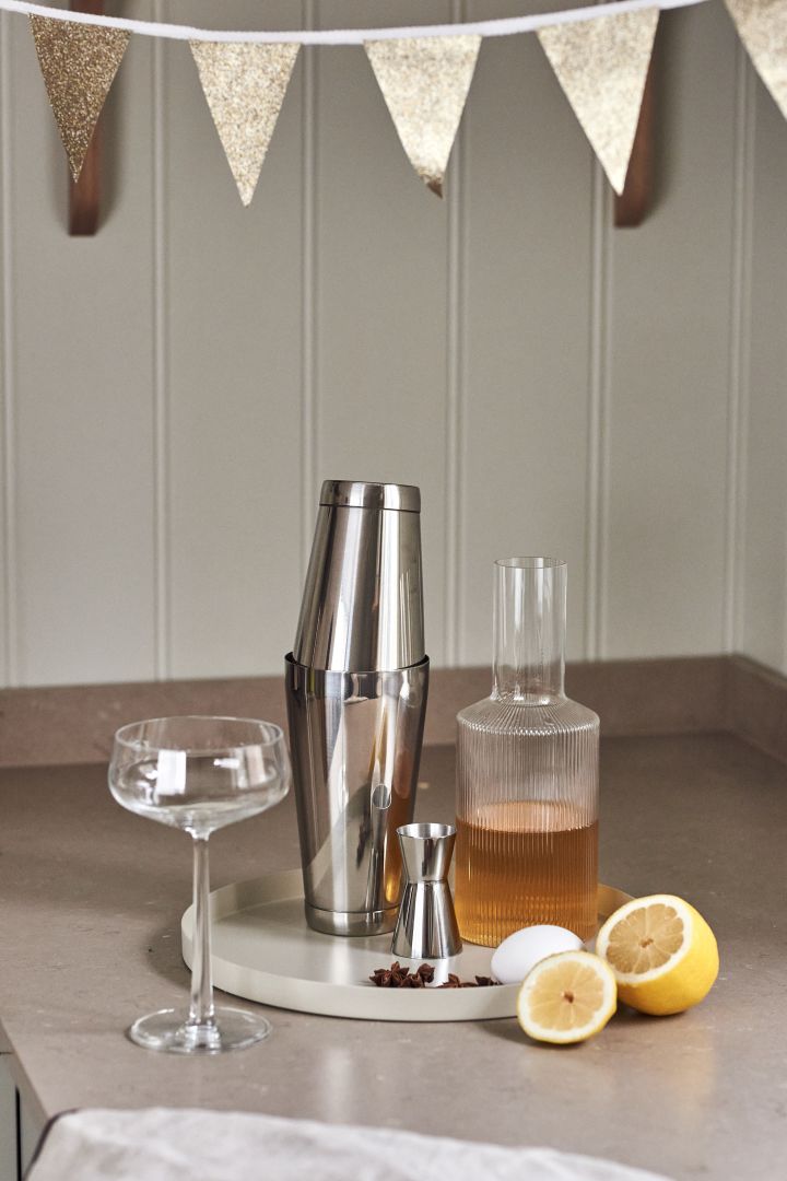 4 recettes de cocktails festifs pour la nouvelle année - Shaker Dorre, verre doseur Rosendahl et carafe Ripple de Ferm Living sur un plateau de Cooee Design.