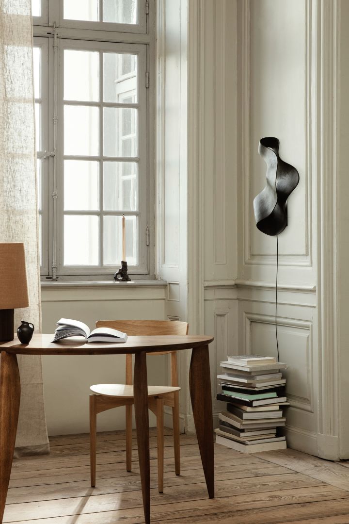 Mettez votre intérieur au goût du jour avec ces idées d'éclairage moderne comme l'applique murale Oyster de Ferm Living. Ici, elle est accrochée au mur au-dessus d'une pile de livres. 