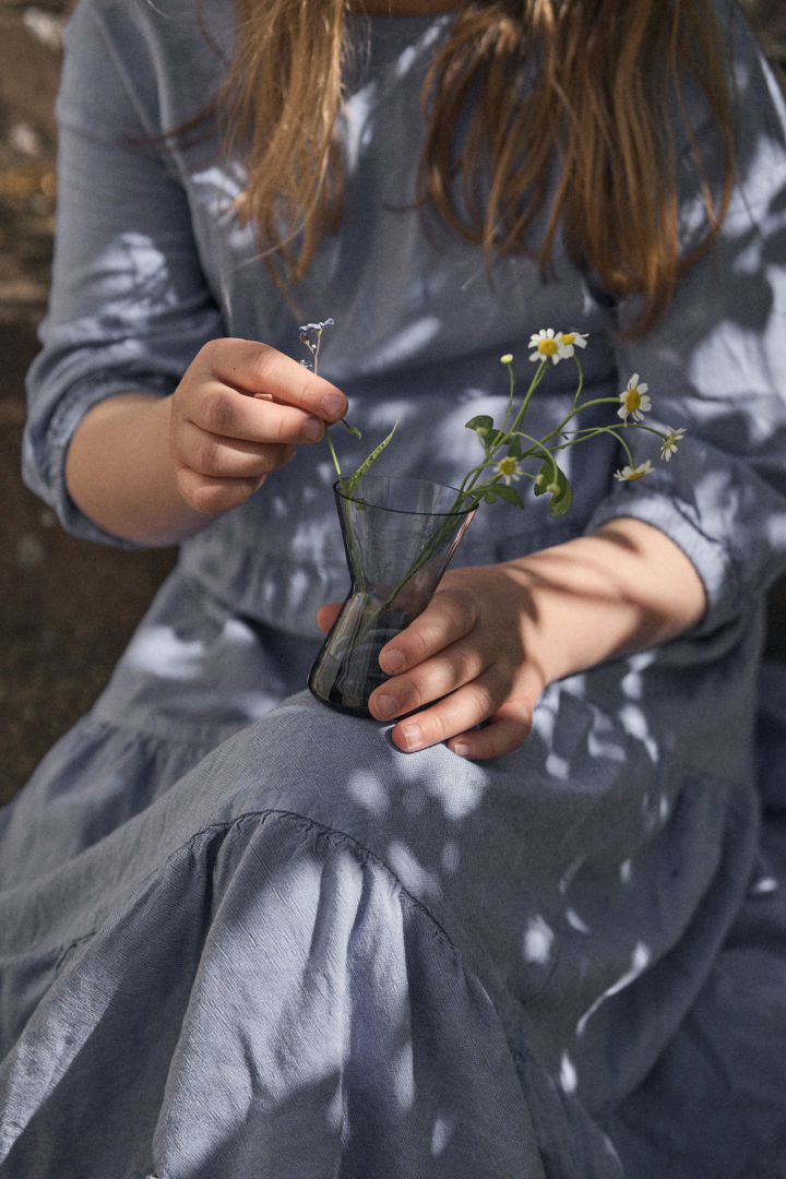 Une jeune fille en robe bleue tiens un mini vase de Orrefors.