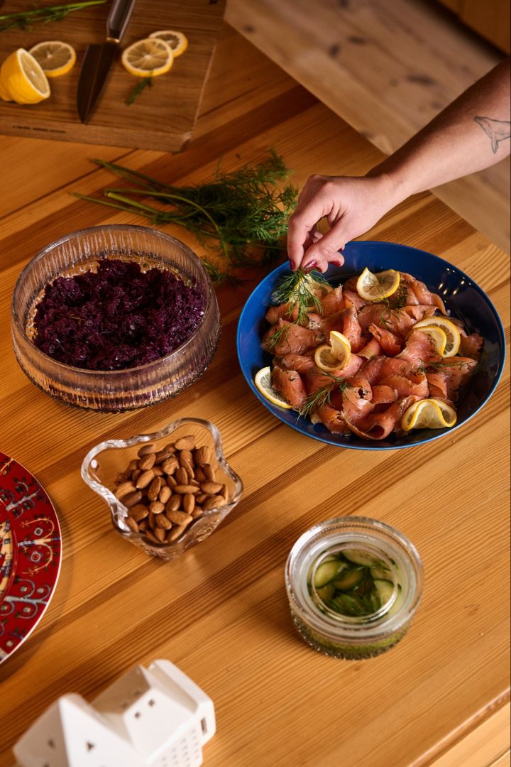 Une main dépose un morceau d'aneth sur une assiette bleue contenant du saumon et du citron, un plat traditionnel dans le cadre d'une célébration de Noël nordique.