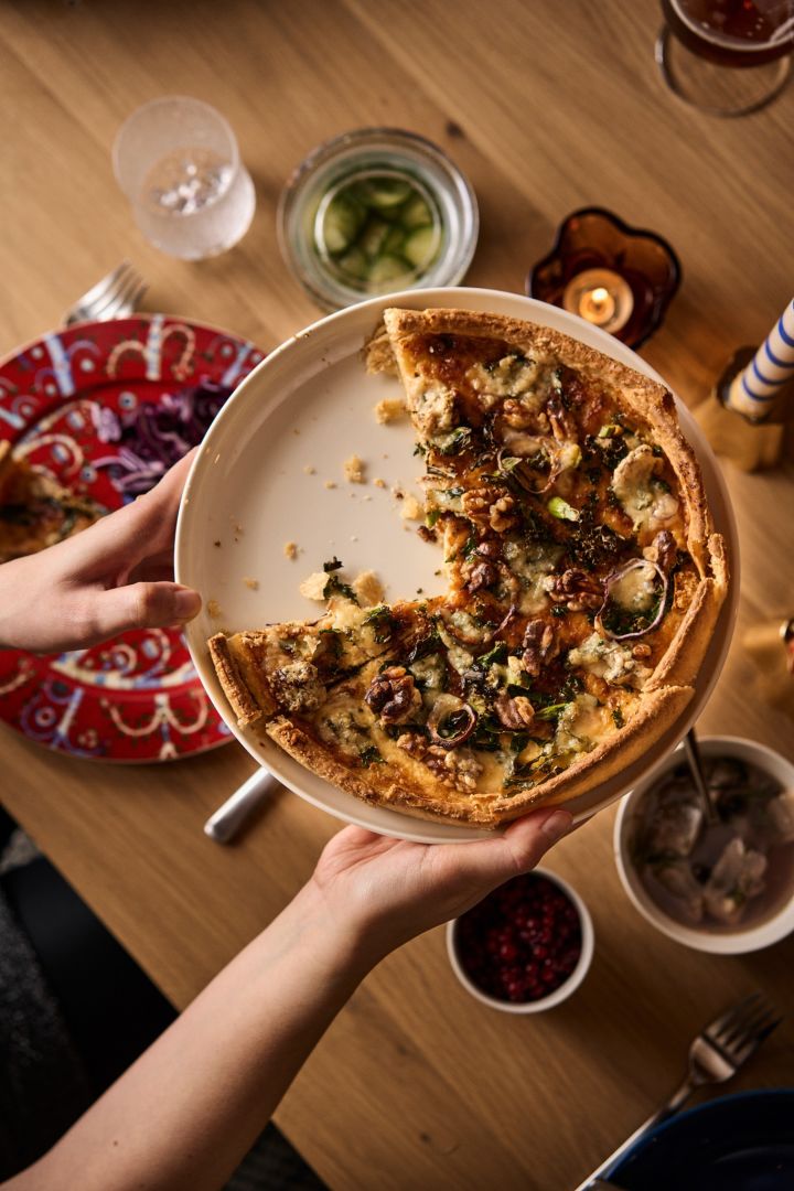 Les mains tiennent une tarte au chou frisé et au fromage dont il manque quelques tranches, un élément traditionnel de la célébration du Noël nordique. 