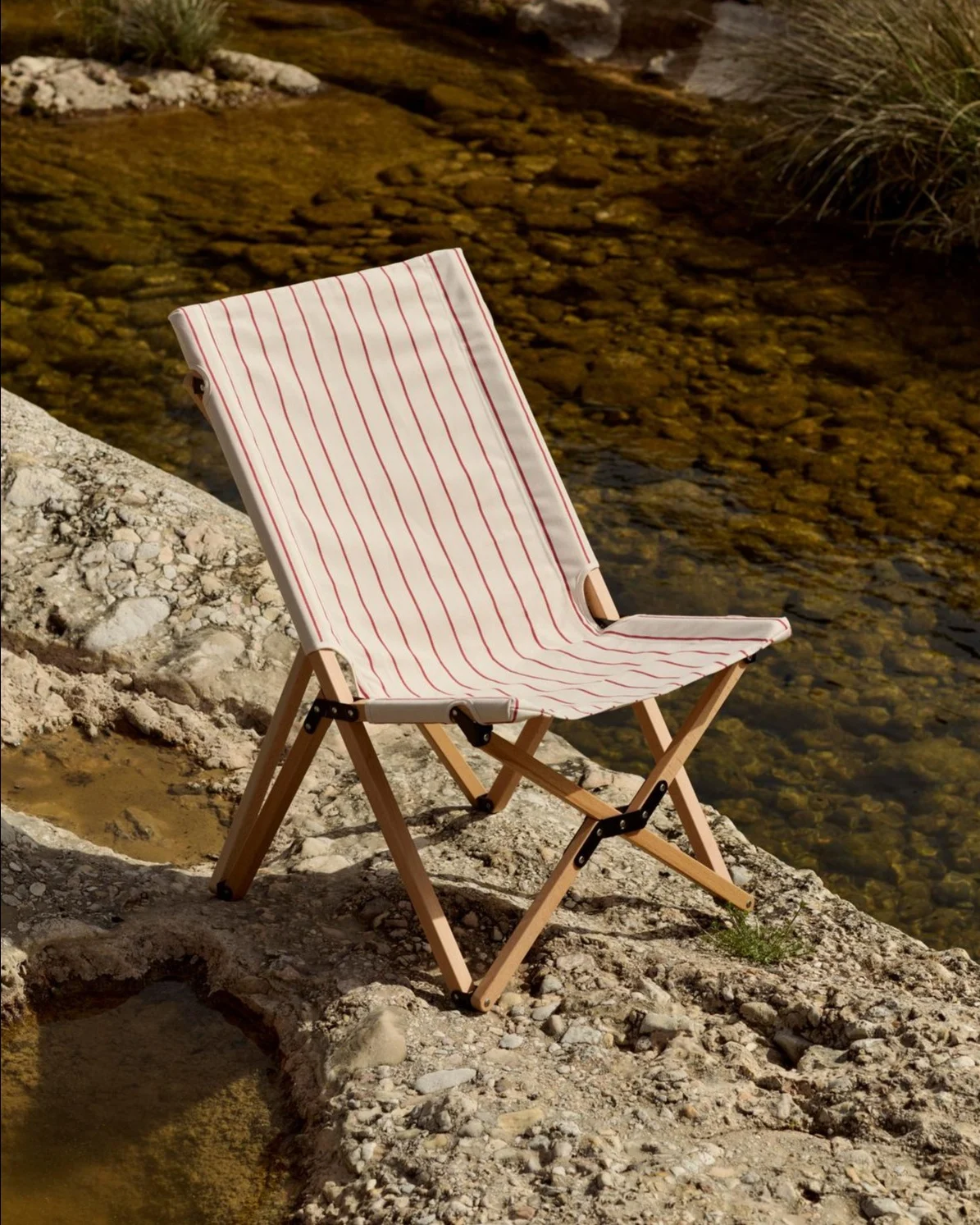 Chaise pliante avec assise en tissu rayé blanc et rouge sur une berge rocheuse au bord d'une rivière.