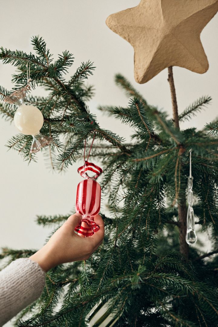 Une main place un gros bonbon emballé dans un arbre de Noël. Une idée de décoration ludique et colorée pour l'arbre de Noël. 