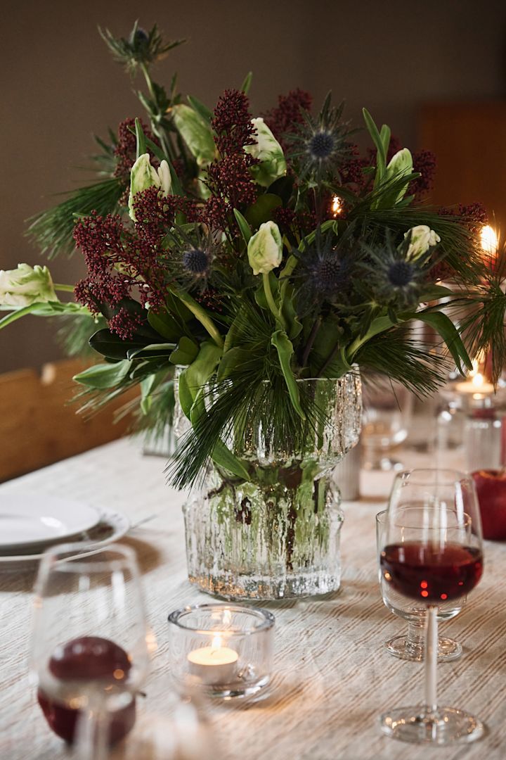 Un vase en verre texturé contenant un bouquet de Noël hivernal est posé sur une table de Noël simple. 