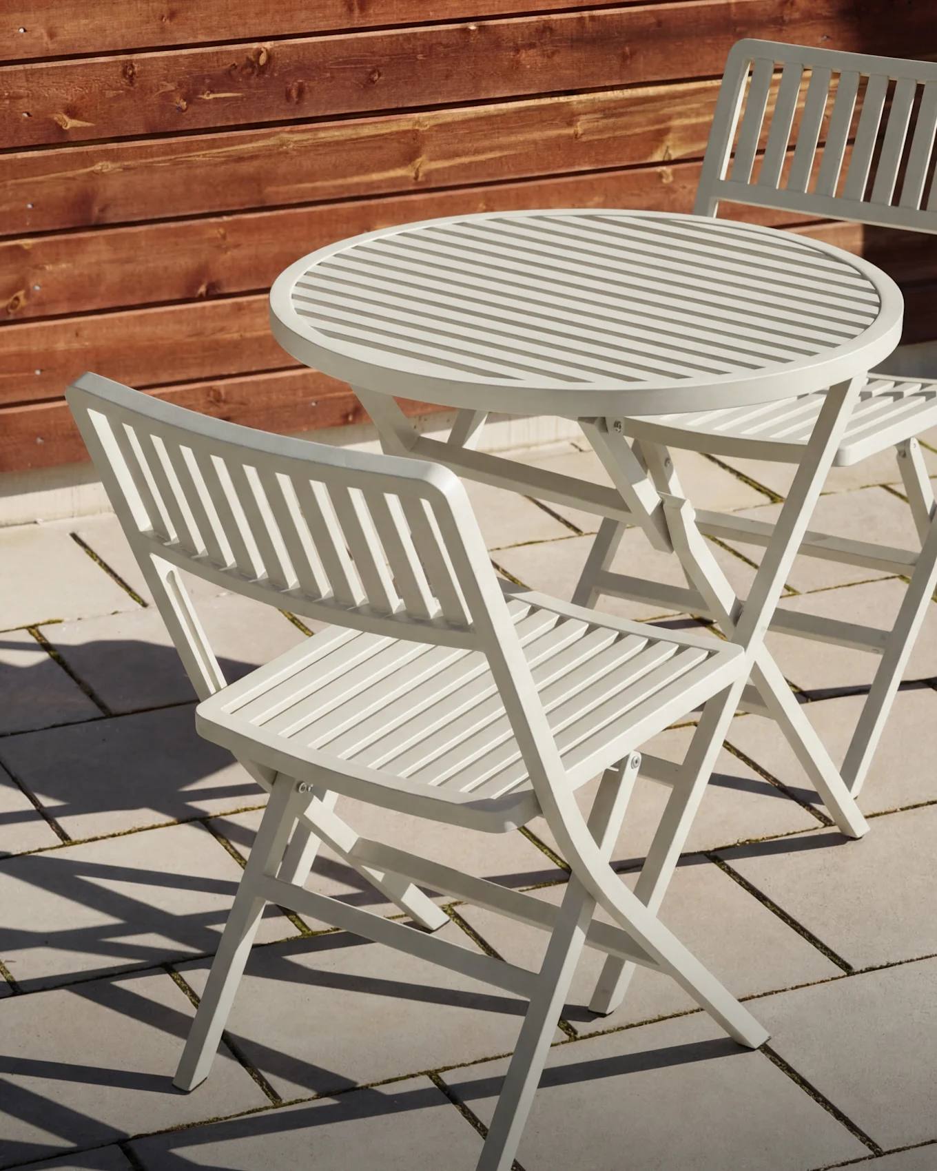 Table d'extérieur à lattes gris clair avec deux chaises pliantes assorties sur un patio.