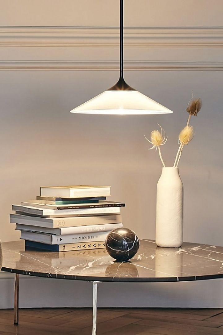 Le plafonnier Orsa d'Artemide est suspendu au-dessus d'une table sur laquelle se trouvent une pile de livres et un vase. 