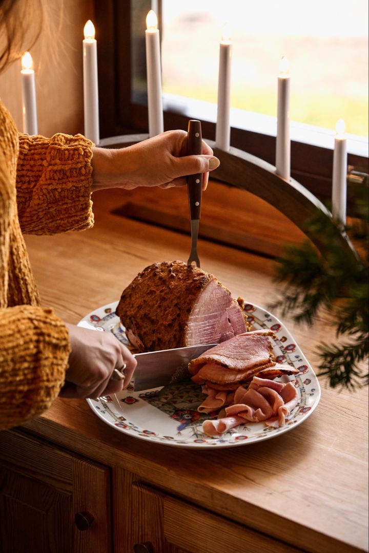 Une femme tranche un jambon traditionnel de Noël nordique dans une vitrine à côté d'une arche de bougies de Noël. 