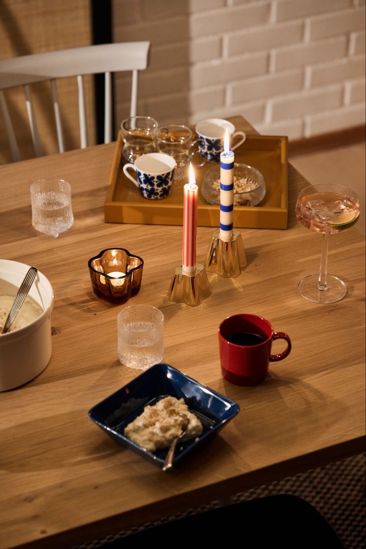 Une table de Noël nordique festive, rouge et bleue, avec un bol bleu contenant du Ris à la Malte, une tasse rouge assortie et des bougies bleues et rouges. 