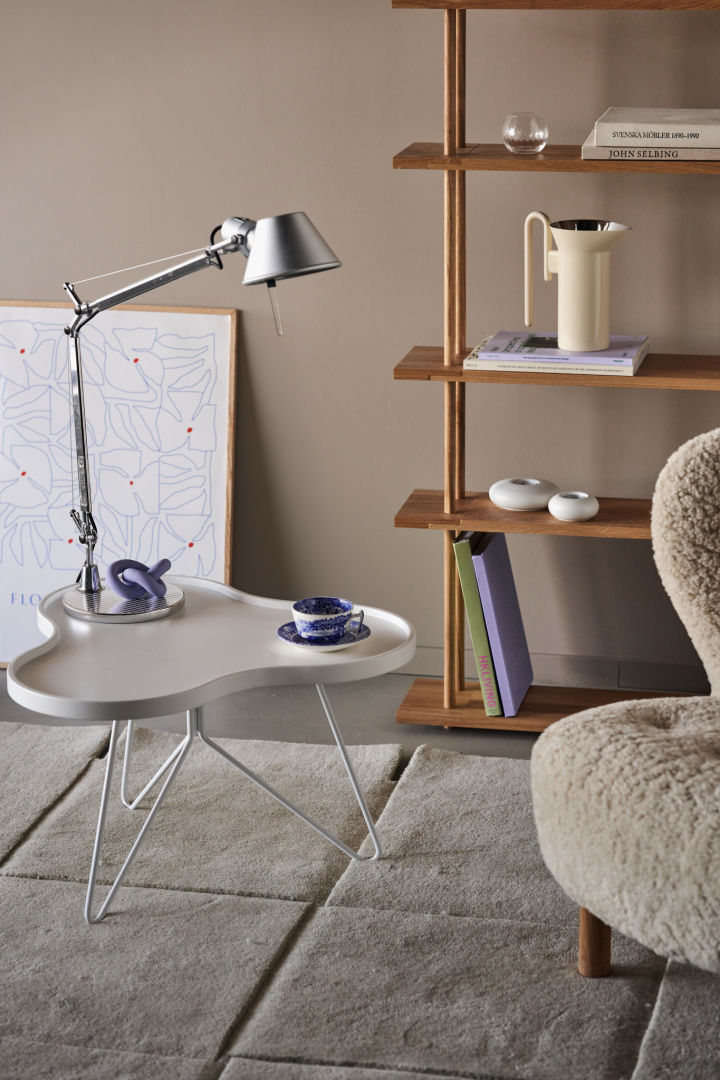 La lampe Tolomeo en acier inoxydable avec un bras réglable est posée sur une table blanche avec des accents violets. 