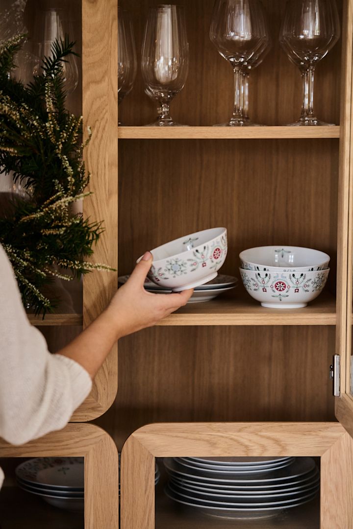 Une main retire d'un placard un bol de Noël à motifs pour le placer sur une table de Noël. 