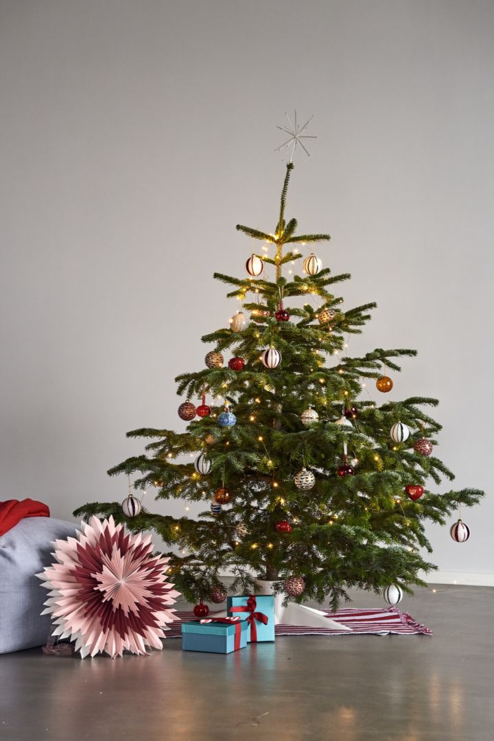 Vous voyez ici un sapin de Noël décoré avec des idées de décoration de sapin de Noël colorées, à côté du sapin se trouve une étoile de Noël rose. 