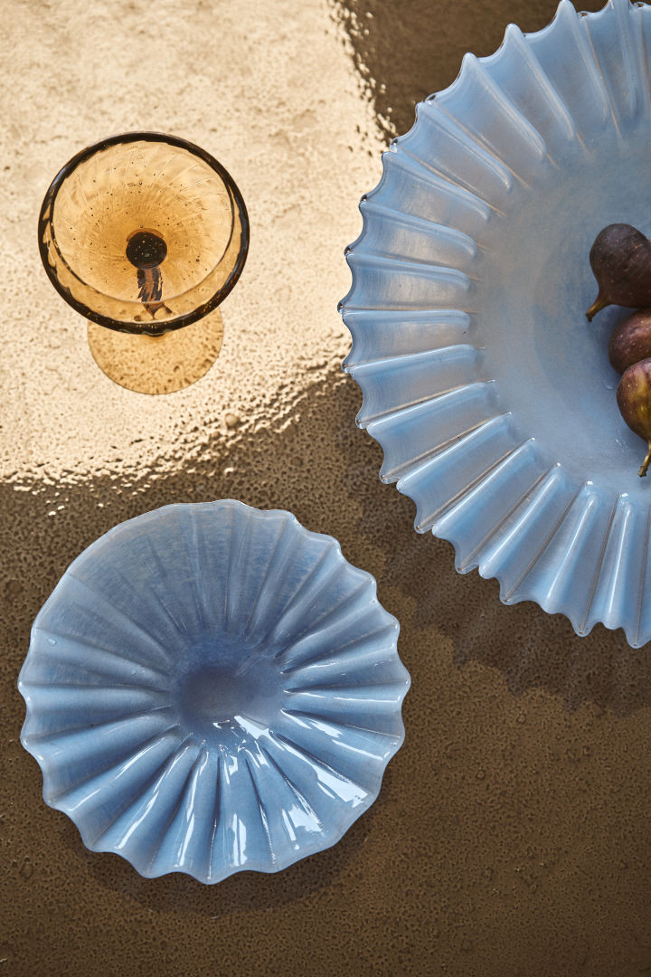 Le bol Lori en bleu clair de Byon présente un magnifique motif plissé en verre coloré, ici à côté du verre à vin Opacity en brun.