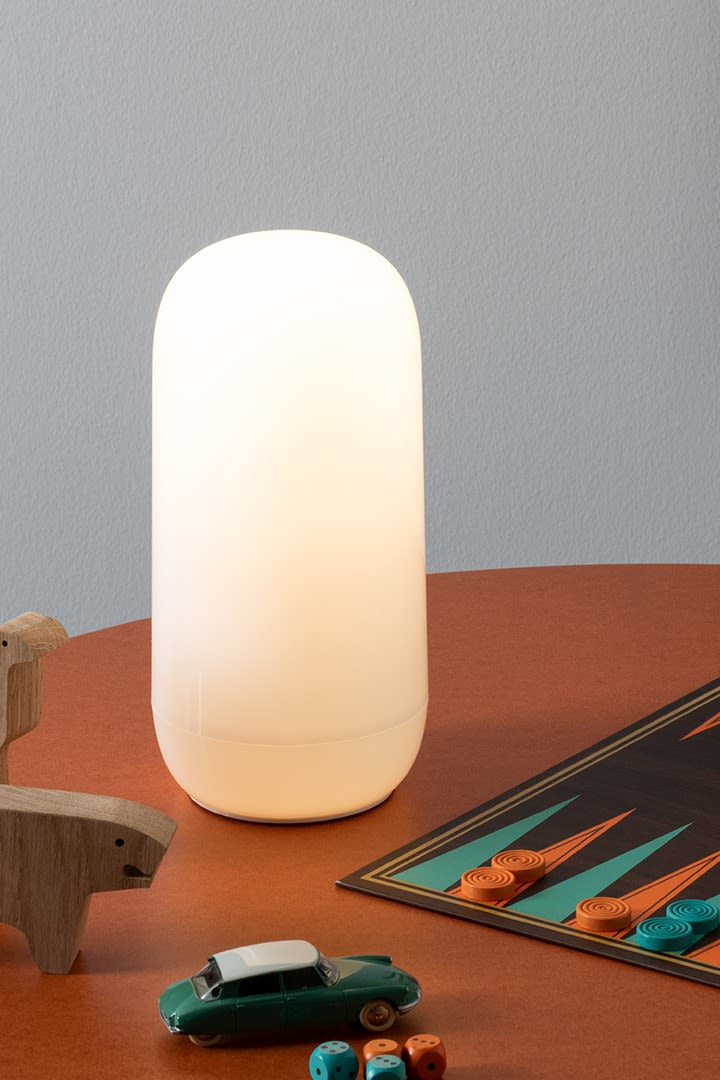 La lampe portable Gople d'Artemide sur un bureau avec des jouets en bois et un jeu de backgammon. 